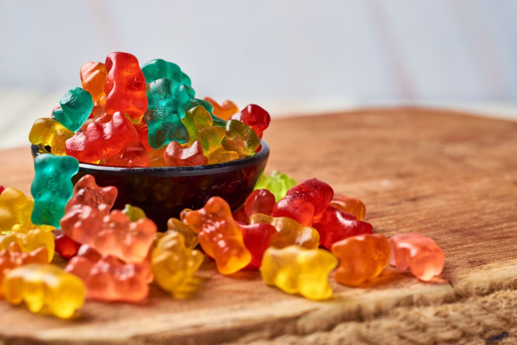 A wooden table showcases a bowl filled with colorful halal melatonin gummies bear