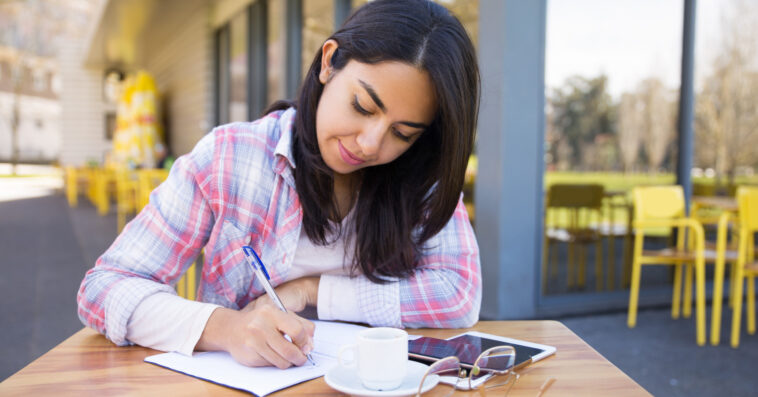 focused young woman making notes outdoor cafe
