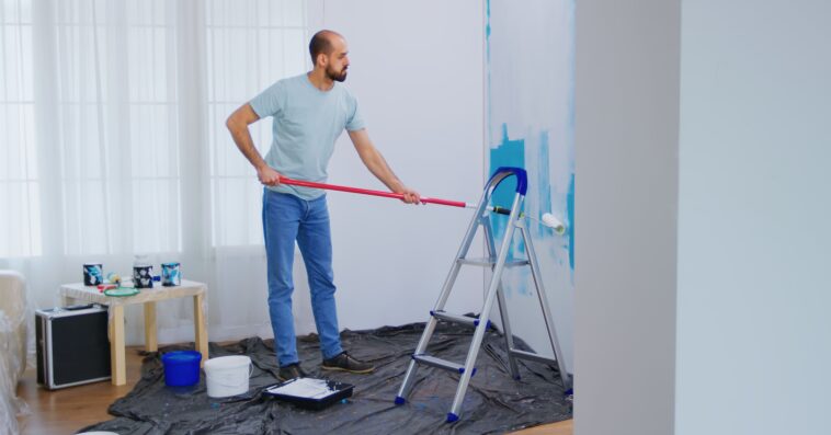 masaking blue paint with roller brush dipped white paint handyman renovating apartment redecoration home construction while renovating improving repair decorating 1