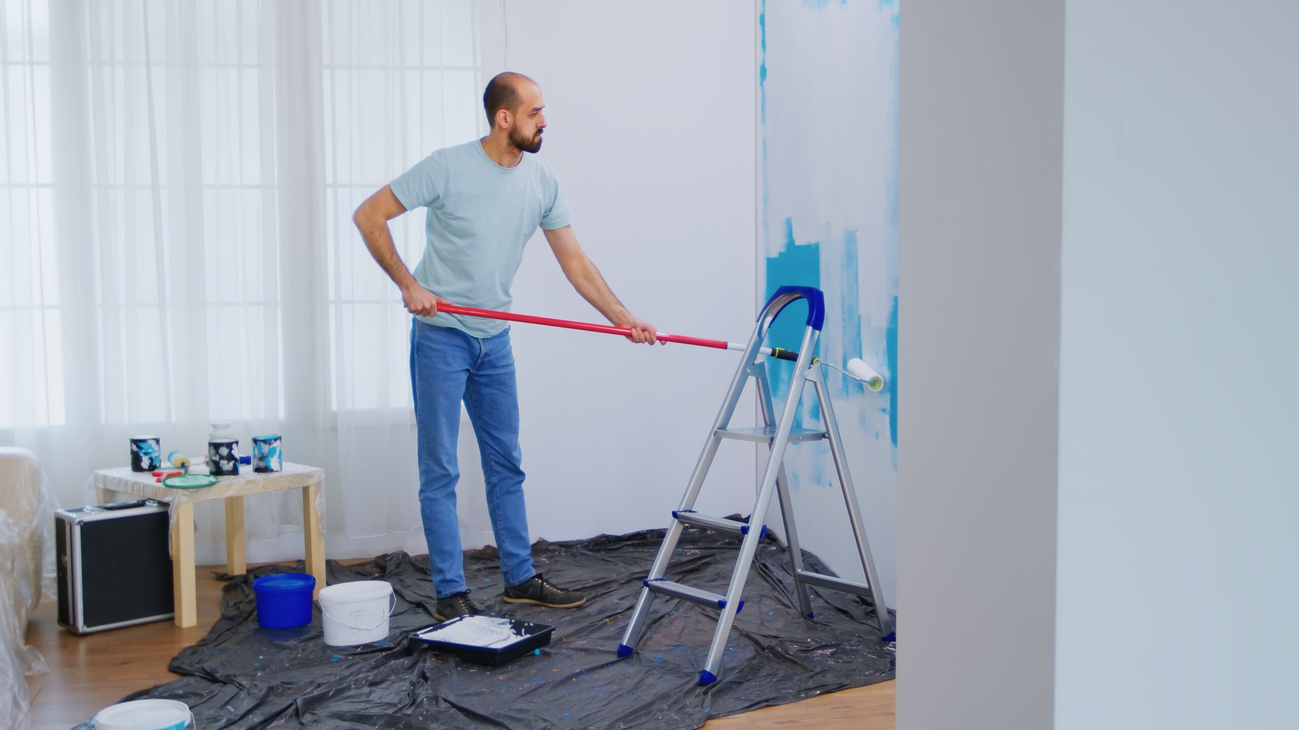 masaking blue paint with roller brush dipped white paint handyman renovating apartment redecoration home construction while renovating improving repair decorating 1 scaled
