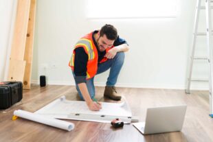 cheerful latin architect smiling while looking online information laptop working construction plans 1
