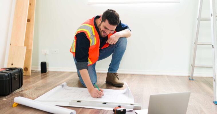 cheerful latin architect smiling while looking online information laptop working construction plans 1
