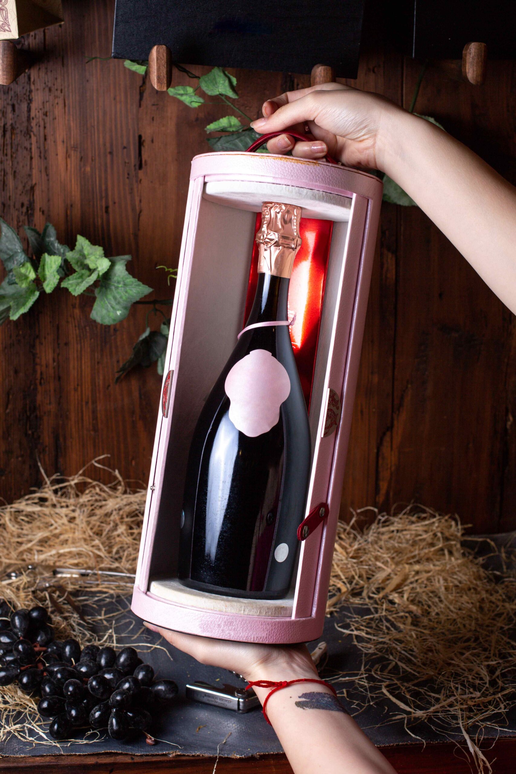 Pinot Noir Rosé Wine – Sip the Sophistication 1 front view black wine bottle inside pink stand held by woman along with black grapes green leaves brown background alcohol winery drink 1 1 1 scaled