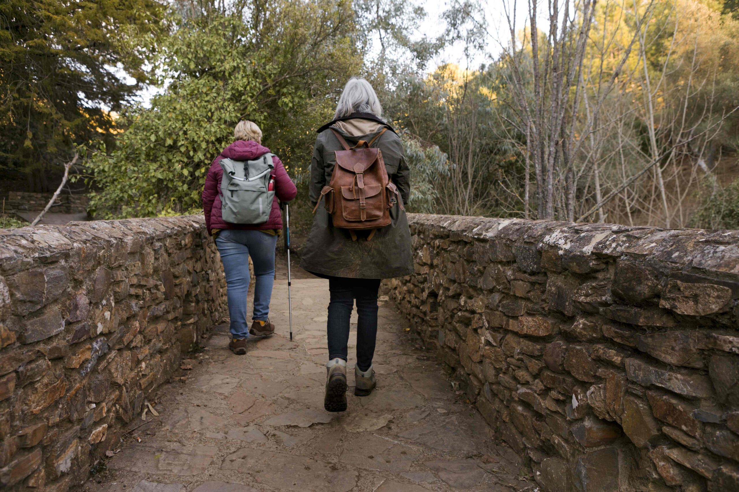 two senior women crossing stone bridge while out nature 1 1 scaled